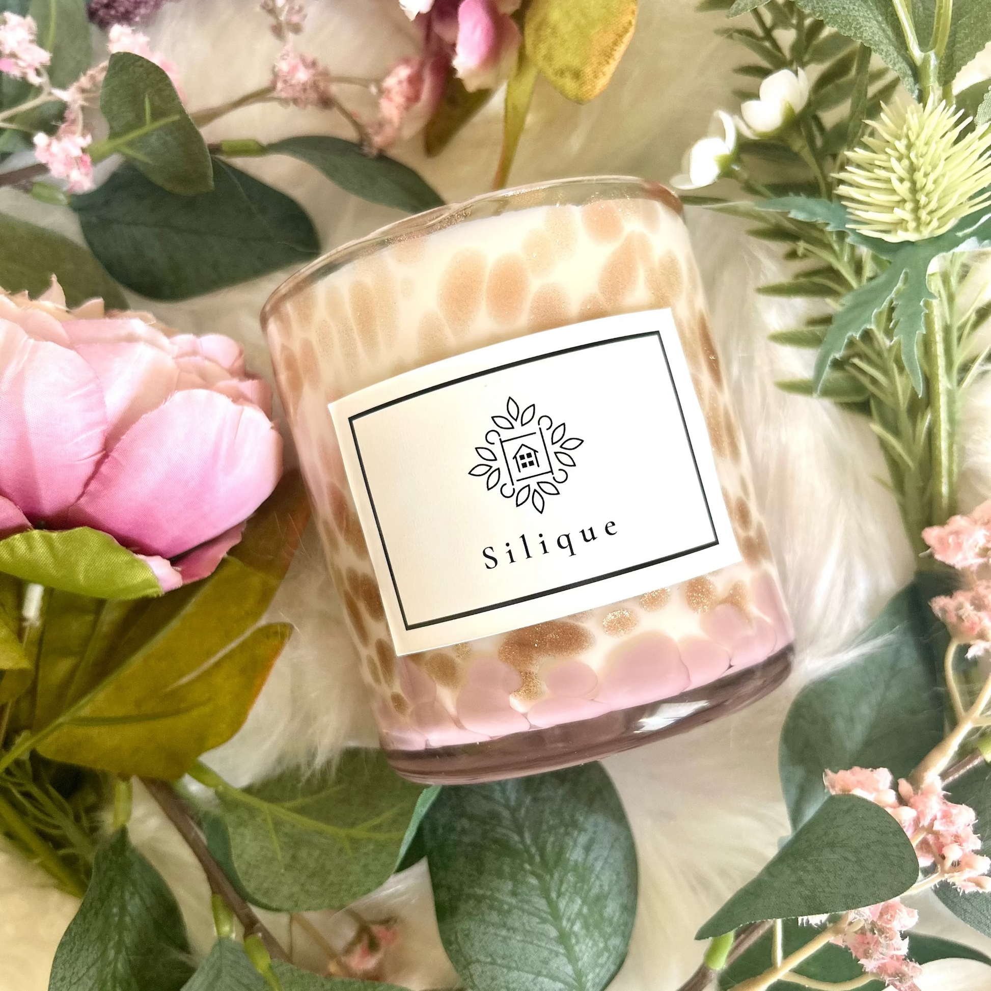 Candle with 'Silique' label surrounded by flowers and greenery